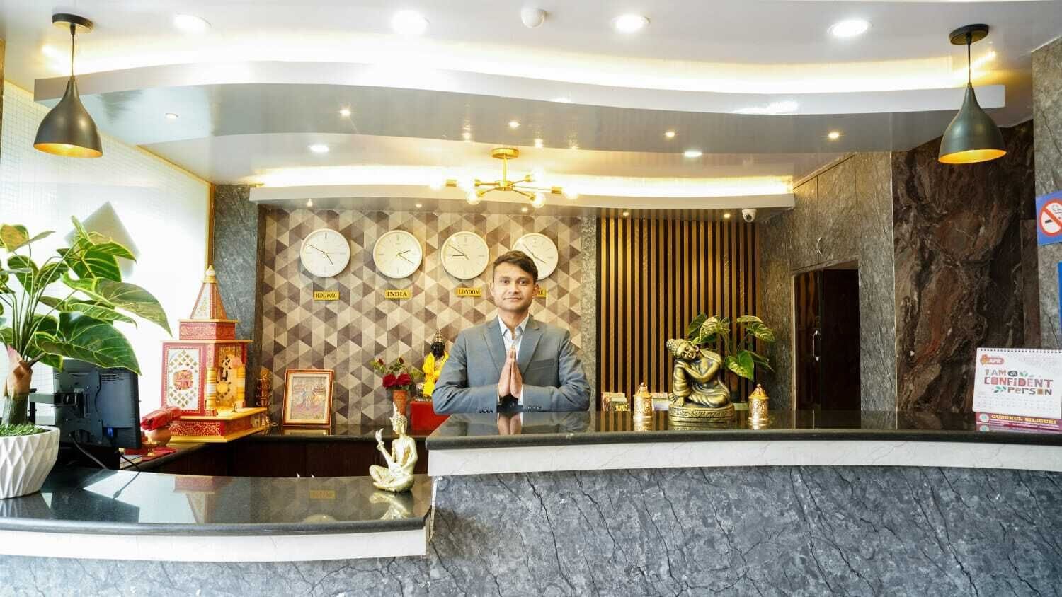 A hotel reception desk with a marble counter, wall clocks, and a decorative Buddha statue.