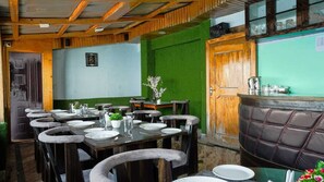 Un restaurante con mesas y sillas de madera, una pared verde y una zona de bar con un asiento acolchado de cuero.