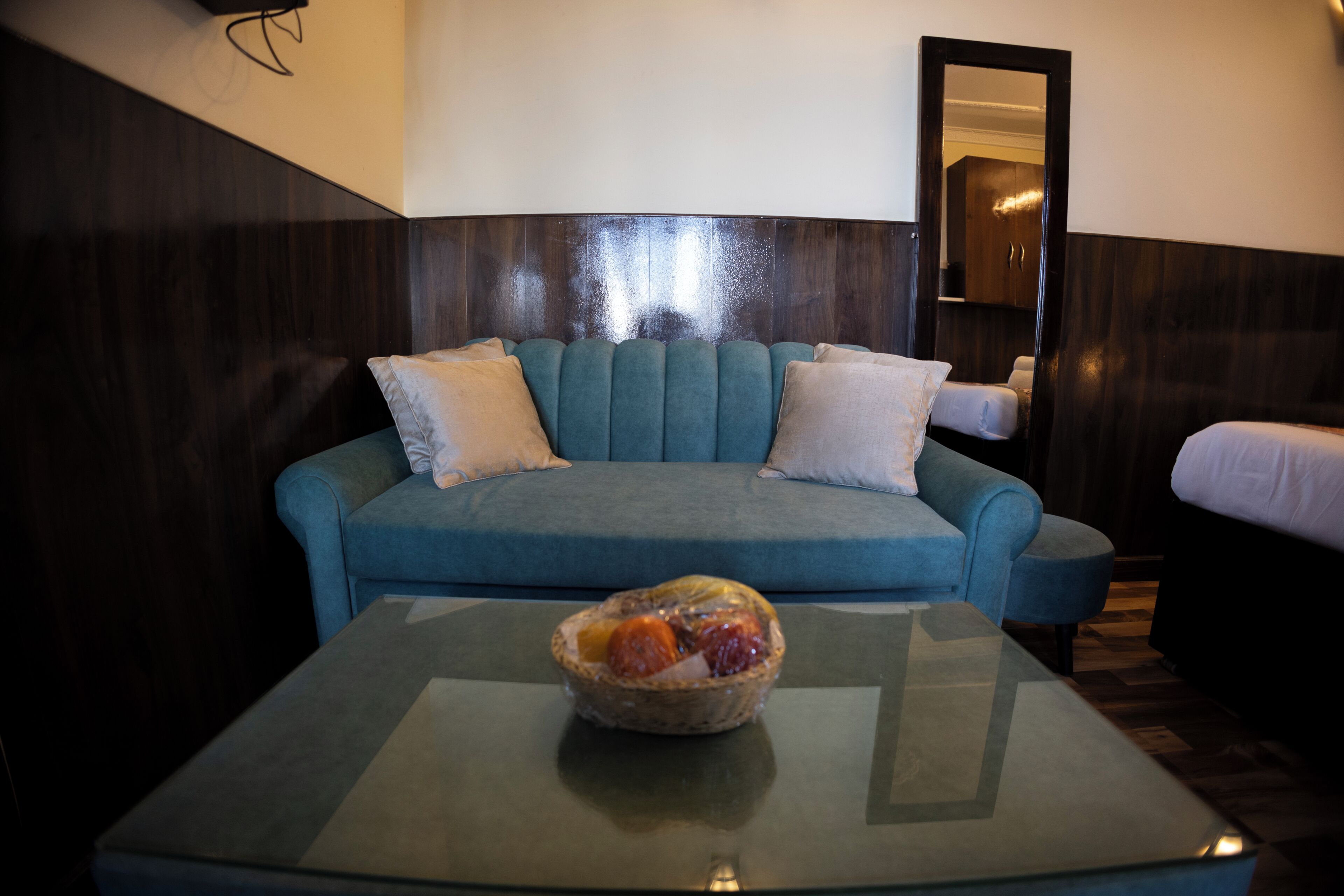 Una habitación con un sofá azul, dos almohadas blancas y una mesa de centro de vidrio con un frutero.