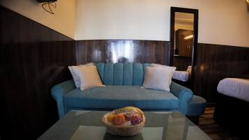 Una habitación con un sofá azul, dos almohadas blancas y una mesa de centro de vidrio con un frutero.