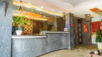 A hotel reception area with marble counters, a plant, and a clock.