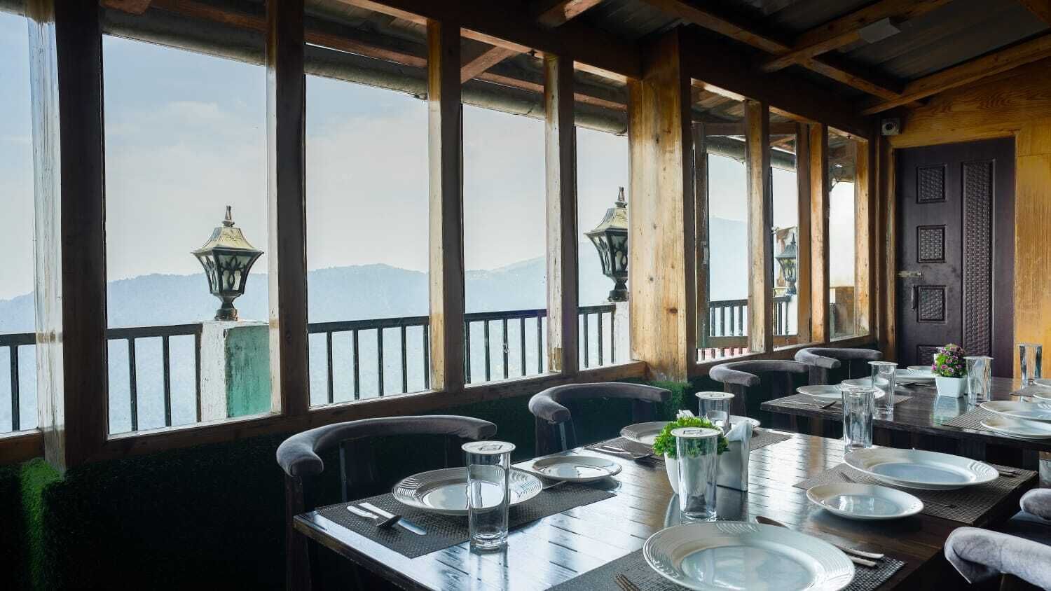 Un restaurant où les tables sont dressées pour le service, de grandes fenêtres offrant une vue sur les montagnes et des lanternes traditionnelles.