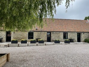 Un bâtiment en pierre avec un toit en tuiles, des places assises à l’extérieur et des jardinières.