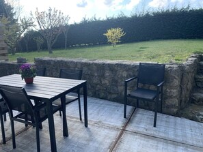 Un espace extérieur aménagé en terrasse, avec une table et des chaises, un mur en pierre et une pelouse verdoyante en arrière-plan.