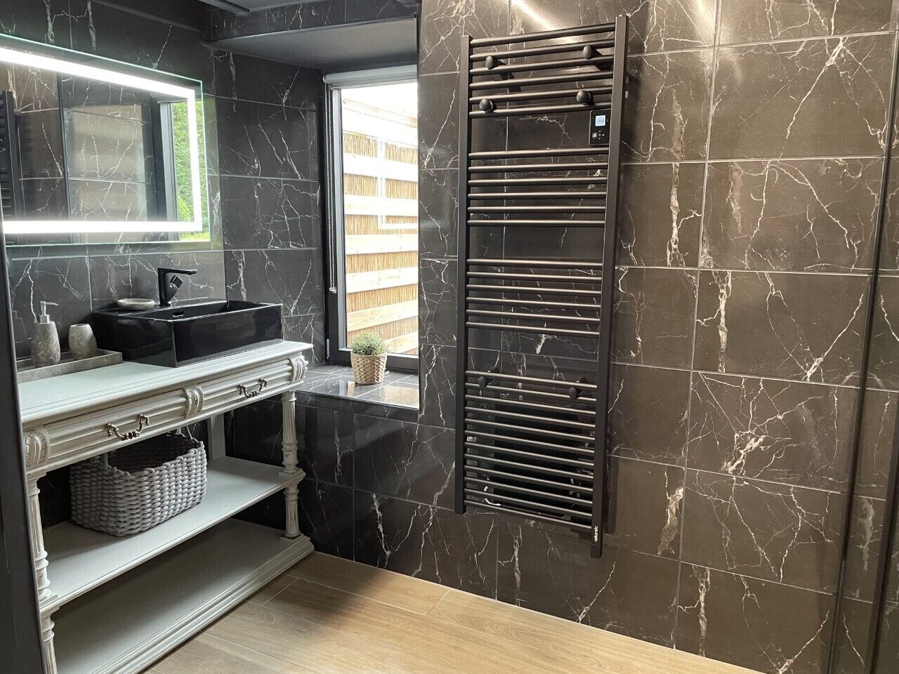 A bathroom with a vanity, mirror, towel rack, and a window with a view of a wooden fence.