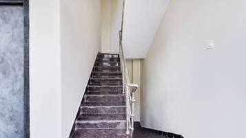 Una escalera con barandilla metálica que lleva a un rellano con un interruptor de luz.