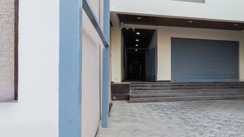 A building entrance with a blue garage door, a set of steps leading up to a dark interior, and a paved driveway.