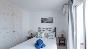 A hotel room with a bed, two bedside tables, a wall-mounted air conditioner, and a window with curtains. - Capuchinos, San Juan de Capistrano (Nerja)