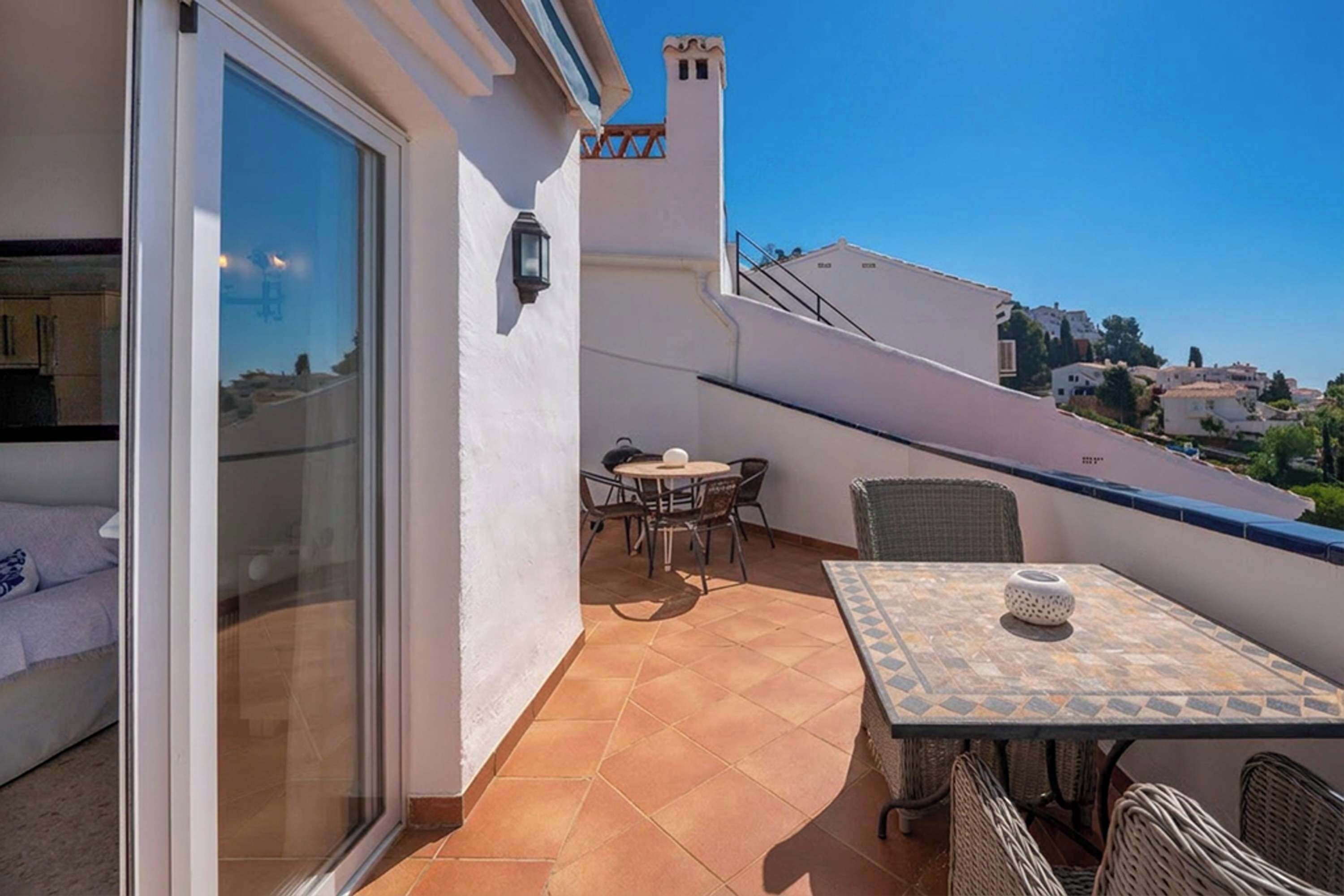 A balcony with a table and chairs, a sofa, and a view of the surrounding area.