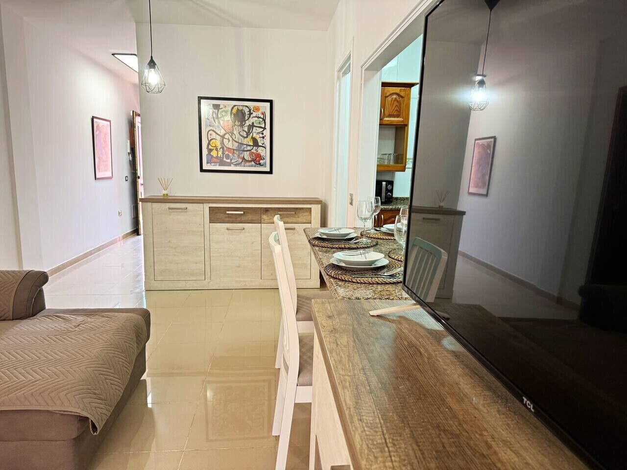 A modern living room with a dining area, a sofa, a TV, and artwork on the walls.