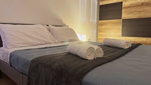 A neatly made bed with a dark blanket and two rolled towels, a wall with a geometric pattern, and a bedside lamp. - Atlantico Apartment: Air Conditioning, Swimming Pool (Santa Cruz de Tenerife)