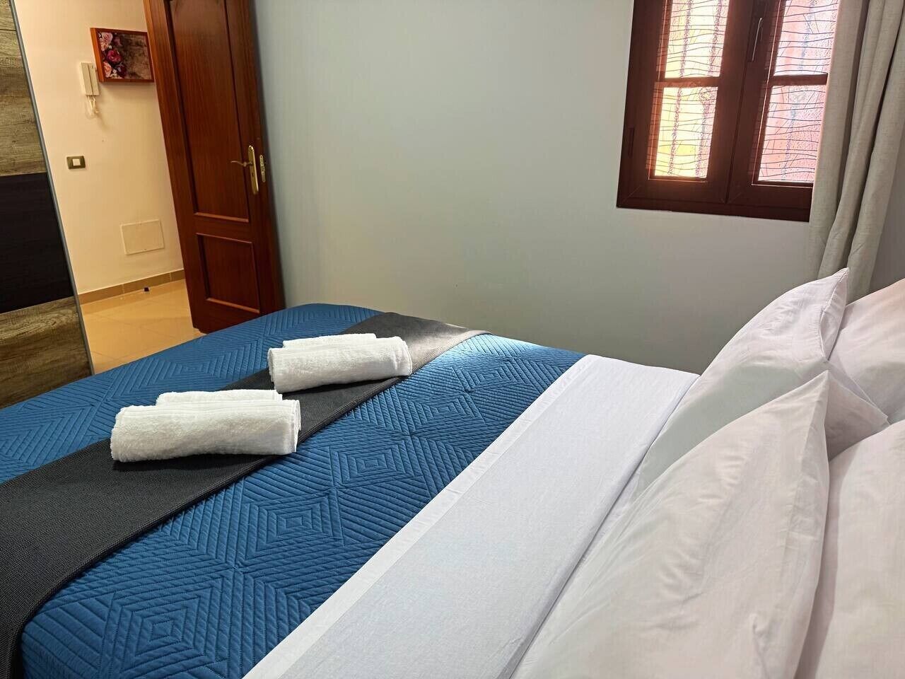 Een bed met een blauwe quilt, witte kussens en twee opgerolde witte handdoeken.