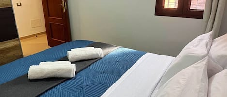 A bed with a blue quilt, white pillows, and two rolled white towels.