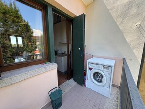 Ein Waschbereich mit Waschmaschine, einem kleinen Fenster und einer Tür zu einem Zimmer.