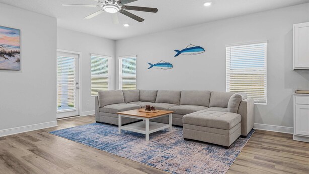 A modern living room with a grey sectional sofa, a coffee table, and a ceiling fan. - Home with Pickleball Courts, Wifi & Beach Essentials (Navarre)