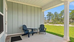 A covered porch with two Adirondack chairs and a small table, overlooking a grassy area with trees. - Home with Pickleball Courts, Wifi & Beach Essentials (Navarre)