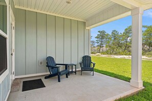 Eine überdachte Veranda mit zwei Adirondack-Stühlen und einem kleinen Tisch, mit Blick auf eine grüne Rasenfläche mit Bäumen.