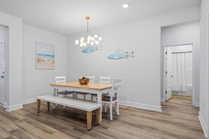 A dining area with a wooden table and chairs, a bench, a wall-mounted light fixture, and two wall decorations of fish. - Home with Pickleball Courts, Wifi & Beach Essentials (Navarre)