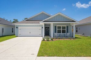 A residential house with a garage, a covered porch with seating, and a well-maintained lawn. - Home with Pickleball Courts, Wifi & Beach Essentials (Navarre)