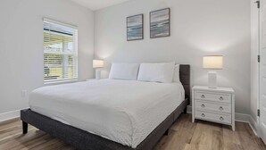 A bedroom with a bed, a nightstand, a lamp, a window with blinds, and two wall-mounted paintings. - Home with Pickleball Courts, Wifi & Beach Essentials (Navarre)