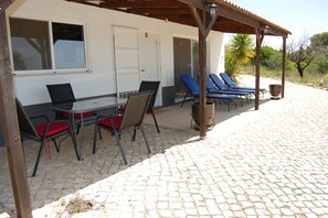 A covered outdoor seating area with a table and chairs, a sheltered patio with lounge chairs, and a building with windows and a door. - Charming Villa With 3 Bedrooms and sea View (Faro)