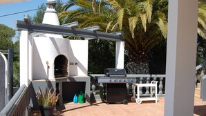 An outdoor patio with a brick floor, a barbecue grill, a pizza oven, and a white pergola structure. - Charming Villa With 3 Bedrooms and sea View (Faro)