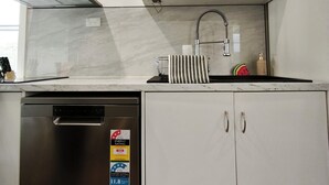 Una cucina con lavastoviglie, cappa aspirante in acciaio inox, mobiletto bianco con etichetta di classificazione energetica e condizionatore integrato.