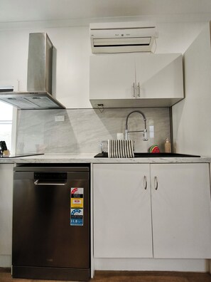 Una cocina con lavavajillas, extractor de acero inoxidable, un armario blanco con etiqueta de clasificación energética y un equipo de aire acondicionado empotrado.