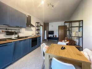 A modern kitchen with blue cabinets, a wooden dining table, and a bookshelf. - Casa Cosette (Lido di Jesolo)