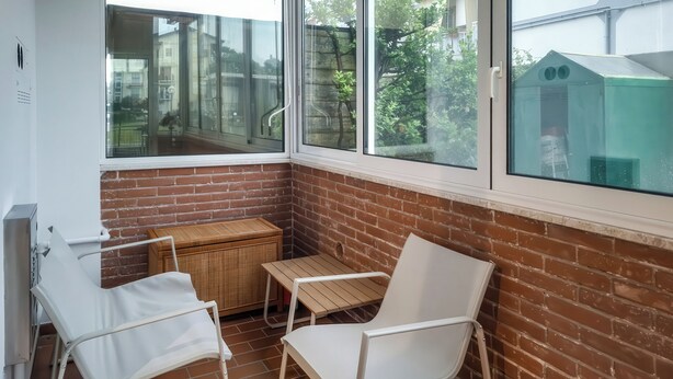 Ein Eckzimmer mit Backsteinwand, Fenster, kleinem Tisch und zwei weißen Stühlen sowie einem Heizkörper.
