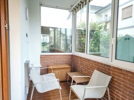 Un piccolo balcone con due sedie bianche, un tavolo di legno e un cesto in vimini.