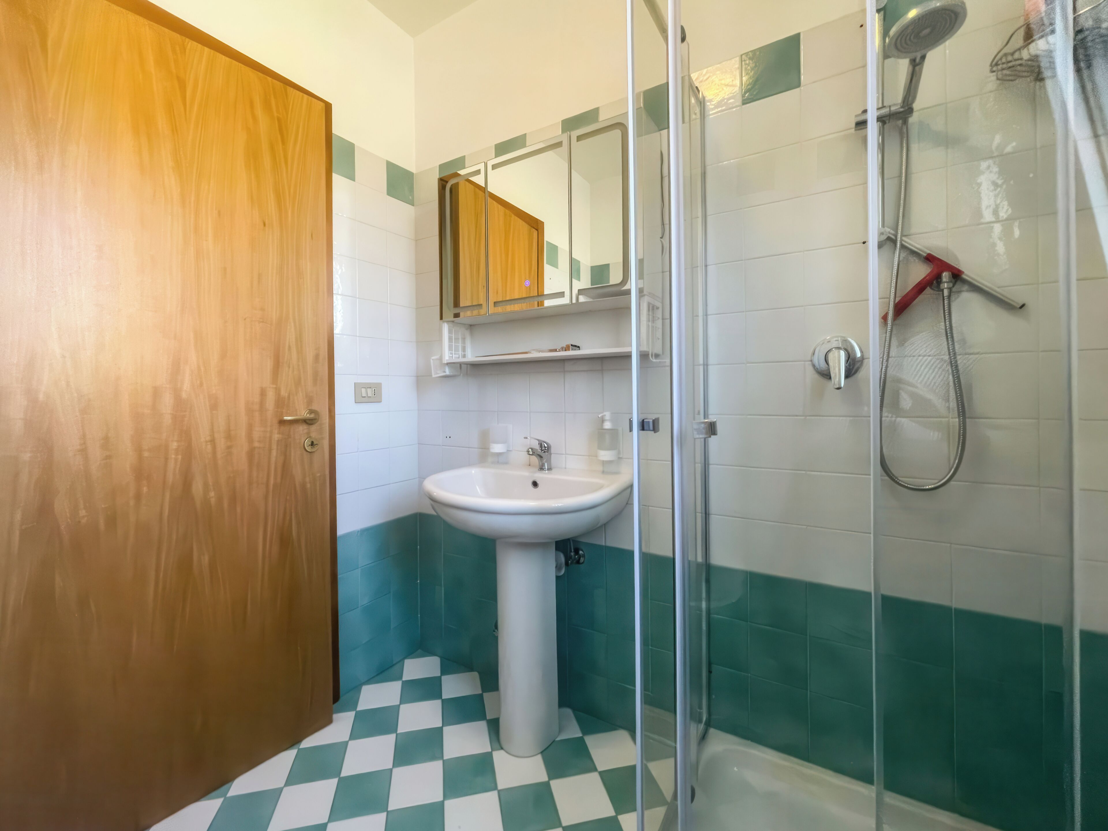 Une salle de bain avec une porte en bois, un lavabo, un miroir et une douche.