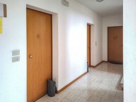 Un corridoio con porte in legno, un cestino e un interruttore a muro.