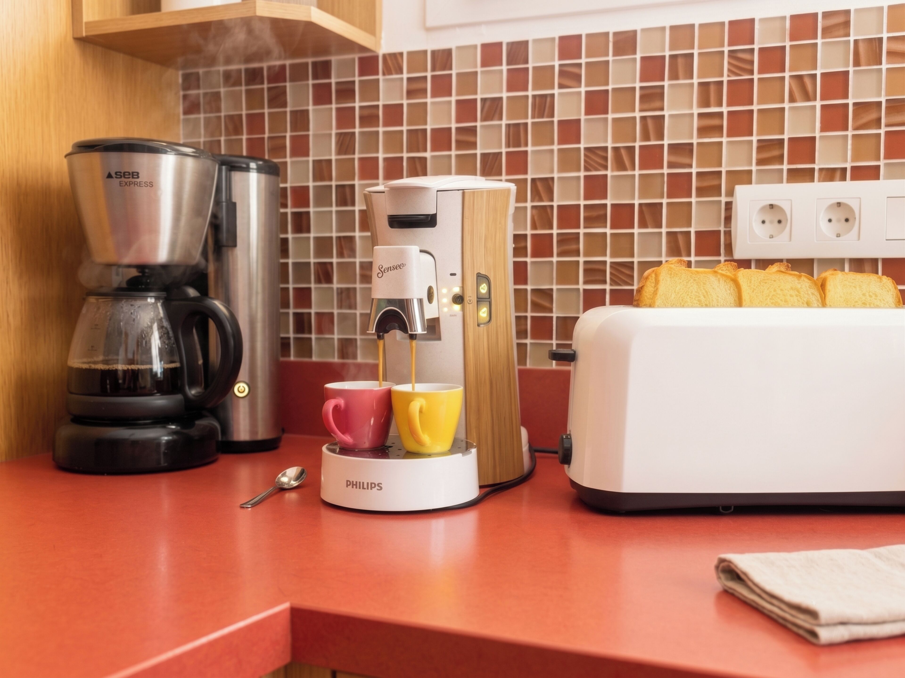 Et køkken med kaffemaskine, brødrister og en brødkasse.