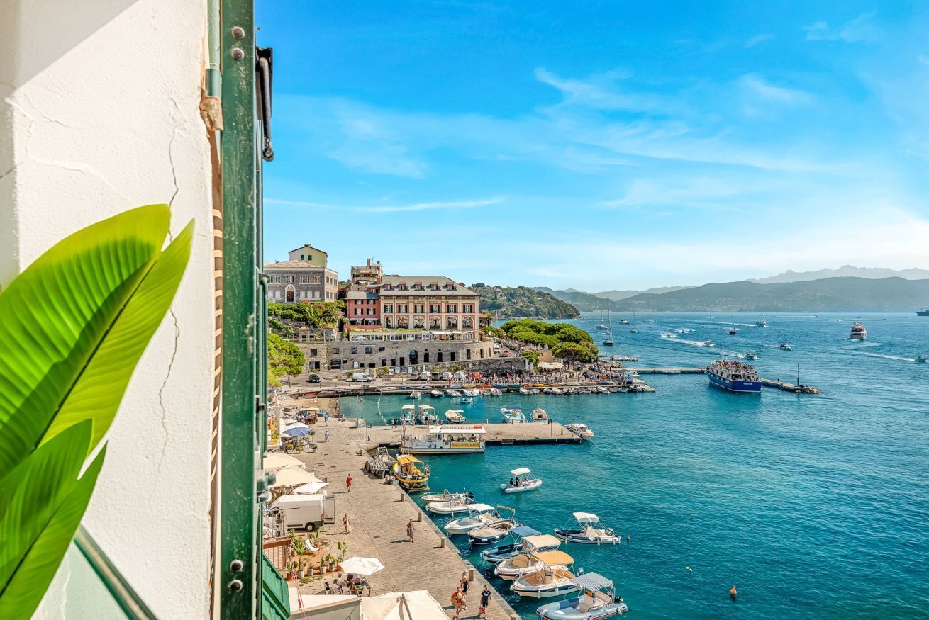 Una cittadina costiera con un porto turistico, imbarcazioni e un grande edificio con numerosi balconi.