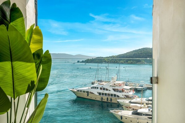Een jachthaven met verschillende jachten die afgemeerd liggen, een heldere blauwe lucht en een bergachtig landschap in de verte.