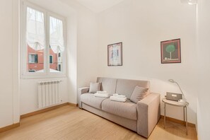 Ein schlicht eingerichteter Raum mit einem beigefarbenen Sofa, einem kleinen Beistelltisch mit einer Lampe und einer Heizung.