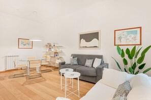 A modern living room with a grey sofa, white armchairs, a small white table, and a bookshelf. - [Atto primo]Central area-Near the station (La Spezia)