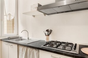 A kitchen with a gas stove, a sink, and a window with curtains. - [Atto primo]Central area-Near the station (La Spezia)