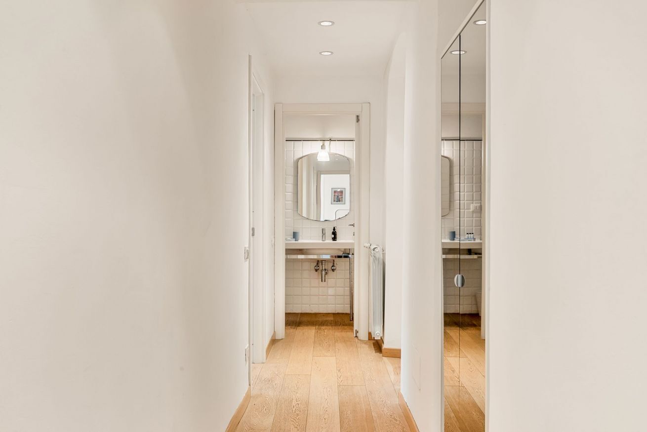 Een gang die leidt naar een badkamer met een spiegel, wastafel en douche.