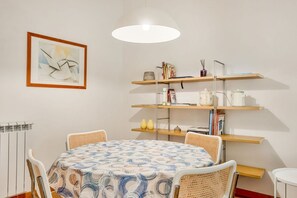 A dining area with a round table, wicker chairs, a patterned tablecloth, a pendant light, and a bookshelf with various items. - [Atto primo]Central area-Near the station (La Spezia)