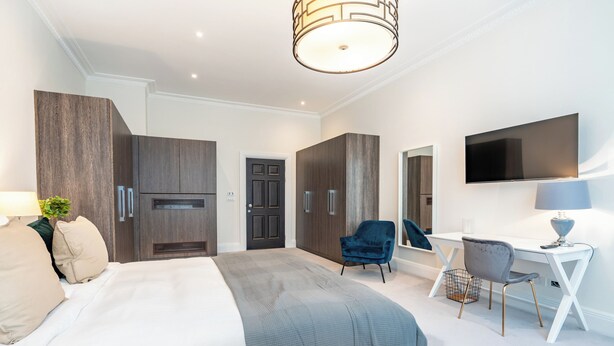 A modern bedroom with a bed, wardrobe, desk, chair, and a TV mounted on the wall. - Fields in Frame at No. 64 (London)