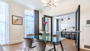 A modern dining area with a glass table, grey upholstered chairs, and a patterned rug. - Fields in Frame at No. 64 (London)
