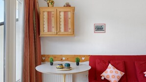 A room with a red sofa, a small round table with decorative items, a wooden cabinet with patterned doors, and a framed picture on the wall. - Superb Mountain View Apartment at the Foot of the Slopes with Large Private Terrace (Villard-de-Lans)