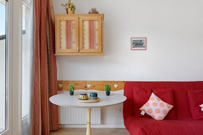 A room with a red sofa, a small round table with decorative items, a wooden cabinet with patterned doors, and a framed picture on the wall.