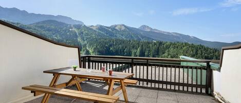 Une table de pique-nique en bois, avec des bancs, sur un balcon donnant sur un paysage montagneux.