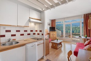 Una cuina moderna amb rentaplats integrat, zona de menjador amb taula i cadires, i una finestra gran amb vista a la muntanya.