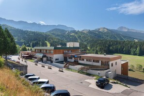 A modern building with a ski resort sign, parking area, and a view of mountains.