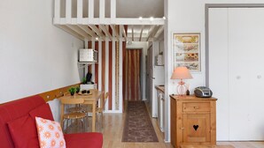 A compact living space with a kitchenette, a dining area, and a red sofa with a floral pillow. - Superb Mountain View Apartment at the Foot of the Slopes with Large Private Terrace (Villard-de-Lans)