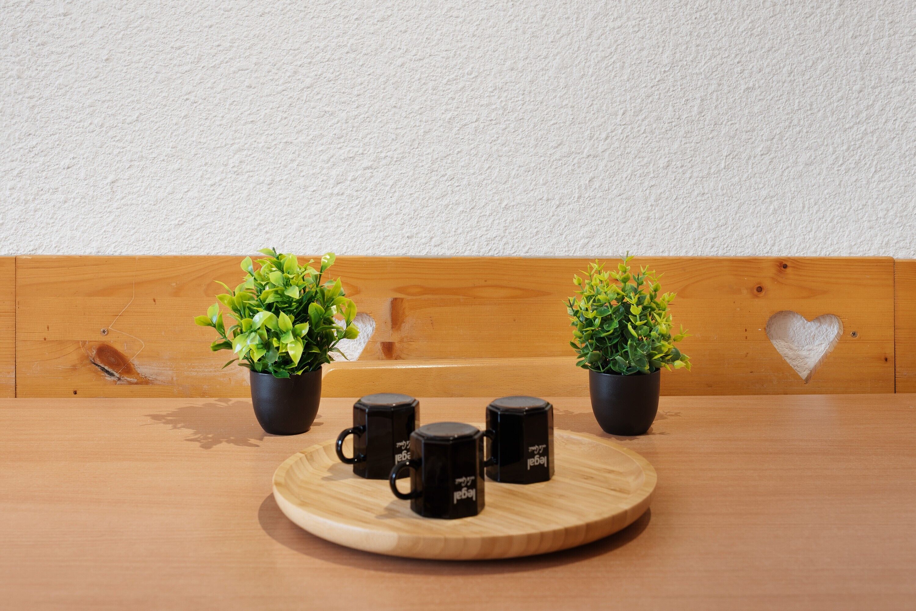 Ein Holztisch mit einem runden Tablett, das schwarze Tassen, zwei Blumentöpfe und eine Holzbank mit Herzförmigem Ausschnitt trägt.